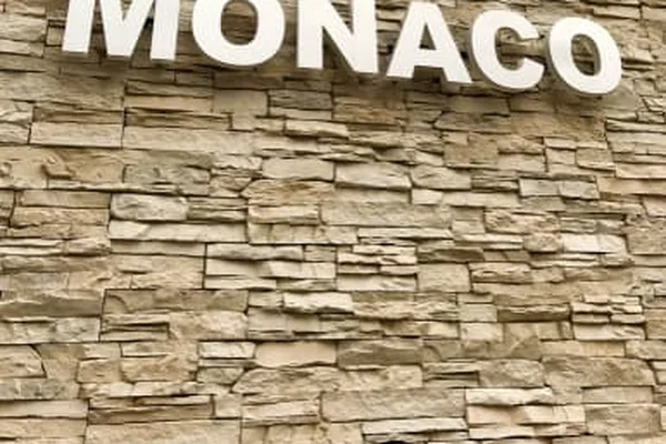 Biały napis "MONACO" na beżowej ścianie z ułożonych kamieni na Lądowisku Helikopterów w Monako.