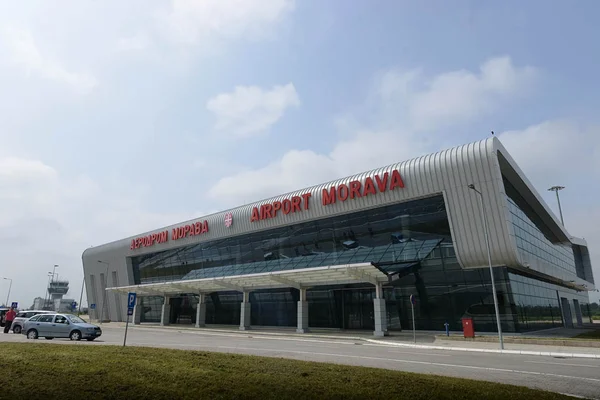 Modern Morava Airport terminal building with curved metal roof and glass facade under blue sky with clouds.