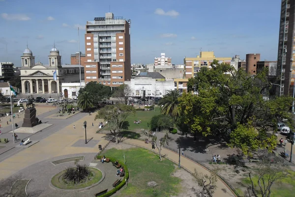 Vista aerea di piazza pubblica con spazi verdi, palme e edifici circostanti urbani.