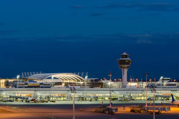 Terminal del Aeropuerto de Múnich al atardecer con edificios iluminados.