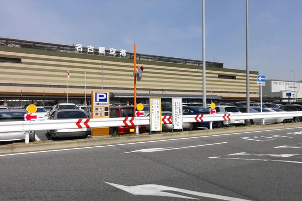 Вход на стоянку в аэропорту Нагоя Комаки с будкой оплаты и многоэтажной парковкой.