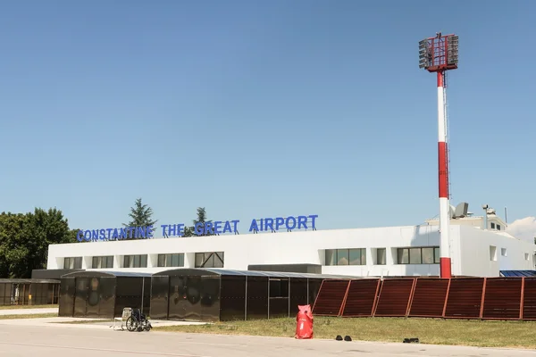 Niš Constantine the Great Airport terminal building with blue signage, red and white lighting tower, and clear sky in the background.