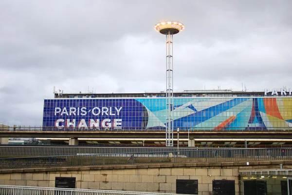 Gran cartel azul "PARIS ORLY CHANGE" con obra de arte abstracta colorida en edificio aeroportuario.