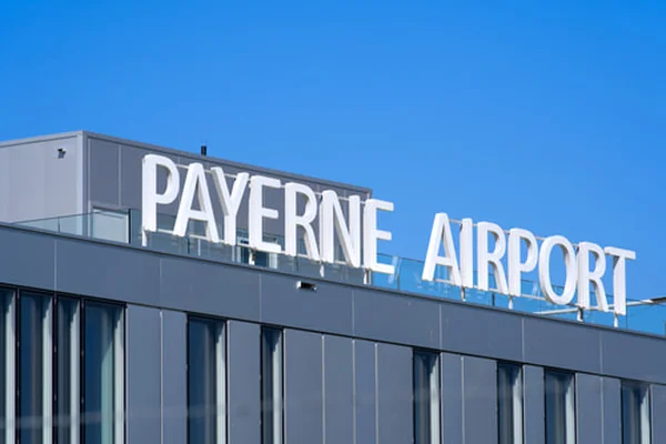 Tablice kierunkowe lotniska Payerne wyświetlane na nowoczesnym szarym budynku na tle czystego błękitnego nieba.
