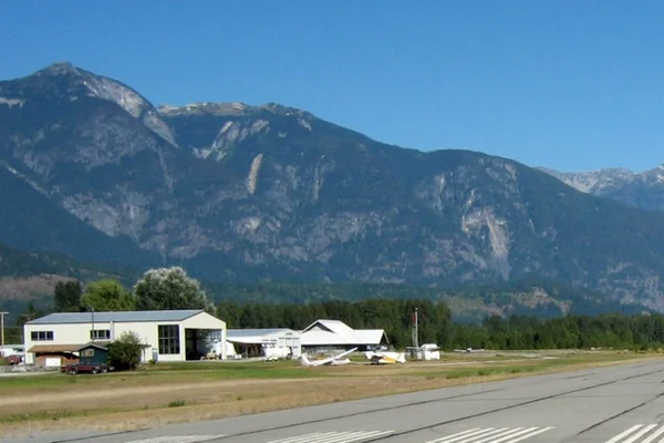Bâtiments blancs et hangars de l'aéroport régional de Pemberton avec montagnes en arrière-plan.