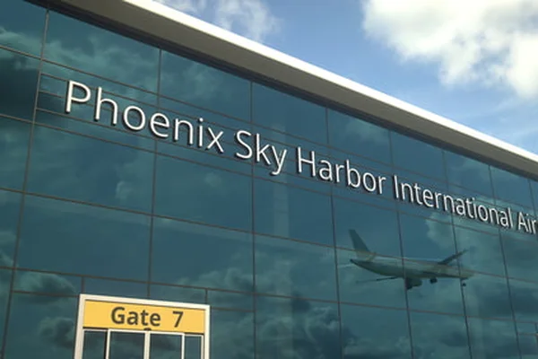 Bâtiment en verre moderne de l'aéroport Sky Harbor Phoenix avec signalisation et avion en reflet.