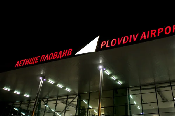 Plovdiv Airport terminal building illuminated at night with red signage displaying the airport name in Cyrillic and English text.