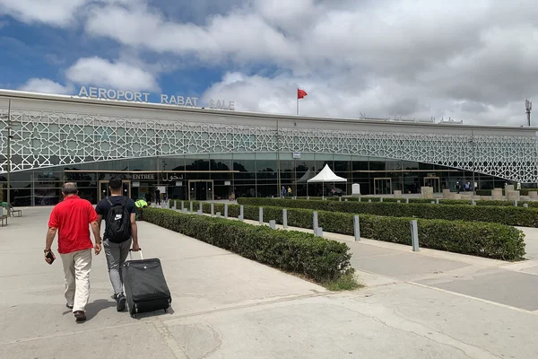 Due viaggiatori camminano verso il moderno terminal dell'Aeroporto di Rabat-Salé con bandiera marocchina.