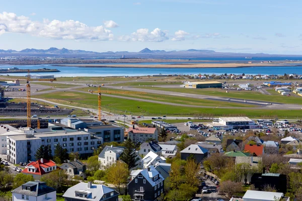 Vue aérienne de l'aéroport de Reykjavik avec pistes, quartiers résidentiels et montagnes en arrière-plan.