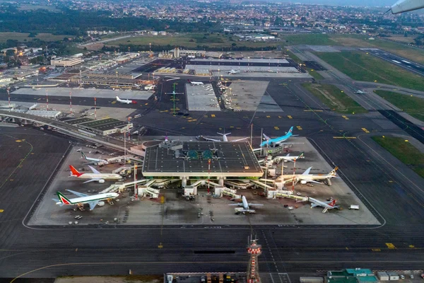 Aerial view of Leonardo da Vinci Rome Fiumicino Airport showing the main terminal building, parked aircraft, taxiways, and surrounding industrial areas.