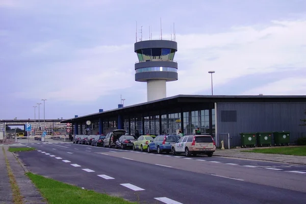 Terminal de l'aéroport de Roskilde avec tour de contrôle et véhicules stationnés sur l'aire durant les heures crépusculaires.