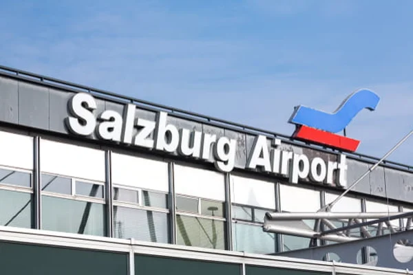 Terminal lotniska Salzburg z napisami i niebieskim logo samolotu na tle czystego błękitnego nieba.