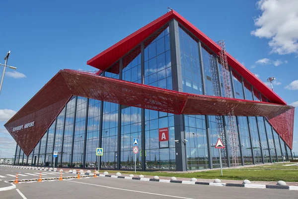 Le terminal moderne de l'aéroport de Saransk, aux murs rouges et vitrés, s'élève sous un ciel bleu nuageux.