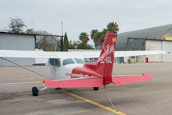 A red and white small aircraft parked at Son Bonet Aerodrome with palm trees and airport buildings visible in the background.