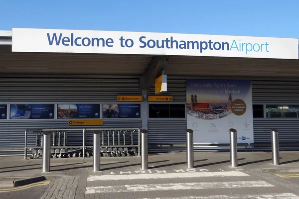 Welcome sign at Southampton Airport entrance with metal barriers and information boards visible under a clear blue sky.