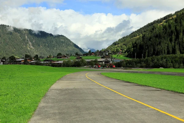 Pista de pequeño aeródromo con línea central amarilla en un valle verde rodeado de montañas.