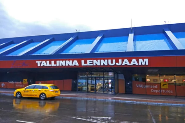 Taxi jaune devant le terminal de l'aéroport de Tallinn avec façade bleue et rouge.
