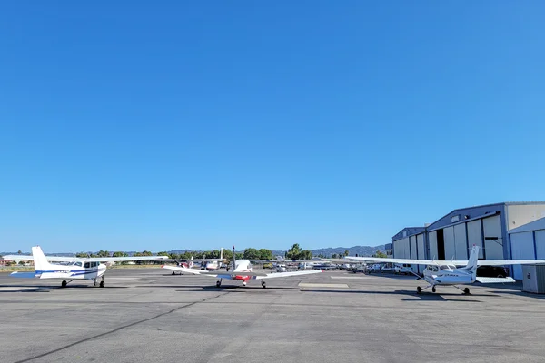 Petits avions garés à l'aéroport de Van Nuys avec hangars et montagnes visibles.