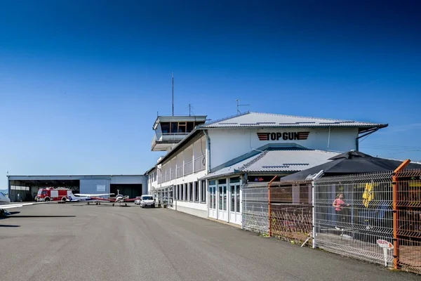 Varaždin Airport terminal building with control tower under clear blue sky, featuring white structure and fenced aircraft parking area.