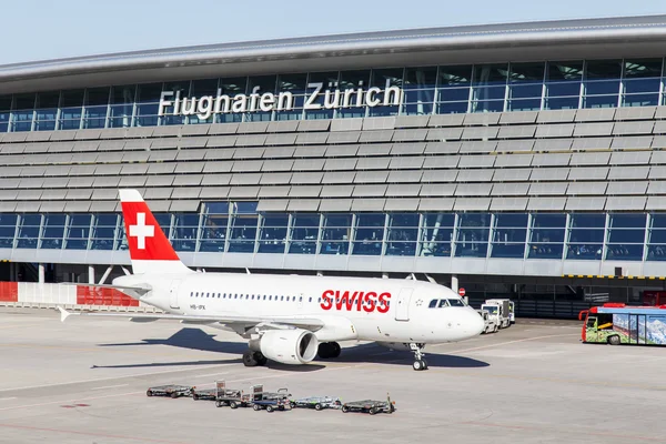 Samolot linii SWISS International Air Lines zaparkowany na Lotnisku Zurychu z budynkiem terminala w tle.