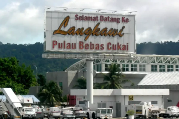 Вывеска аэропорта Лангкави с припаркованными самолётами и горами на фоне.