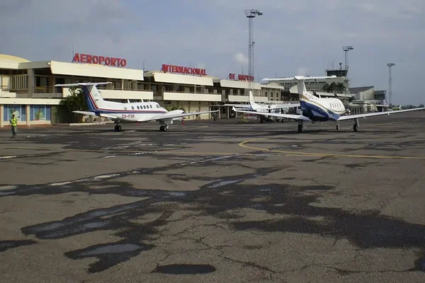 Terminale dell'aeroporto di Maputo con aereo al gate e mezzi sul piazzale sotto cielo nuvoloso.
