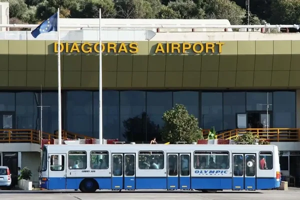 A blue and white tram stops in front of Rhodes Diagoras Airport terminal building.