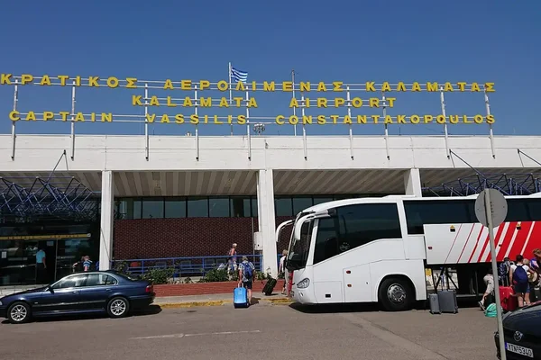 Exterior view of Kalamata Airport entrance with signage, featuring a dark car and white bus parked in front of the modern building facade.