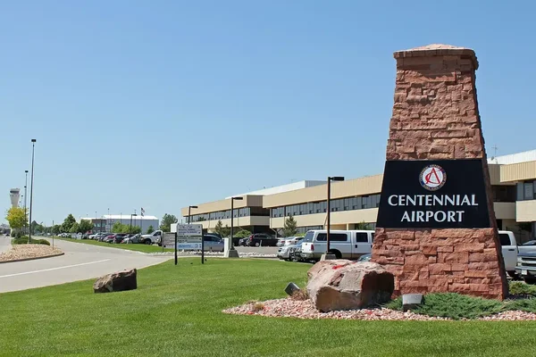 Panneau d'entrée de l'aéroport Centennial avec monument de brique et terminal visible.