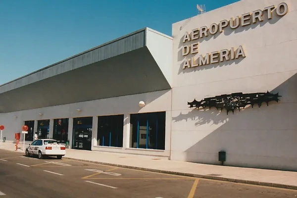 Exterior view of Almería Airport terminal building with white facade and blue signage under clear sky.