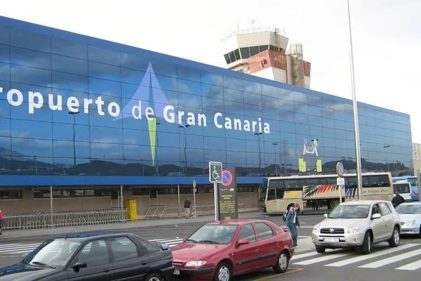 Exterior view of Gran Canaria Airport terminal building with blue facade and parked vehicles in front.