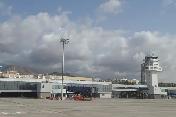 Exterior view of Tenerife Sur Airport terminal building with modern architecture, featuring the airport name on the roof and ground-level service vehicles parked below.