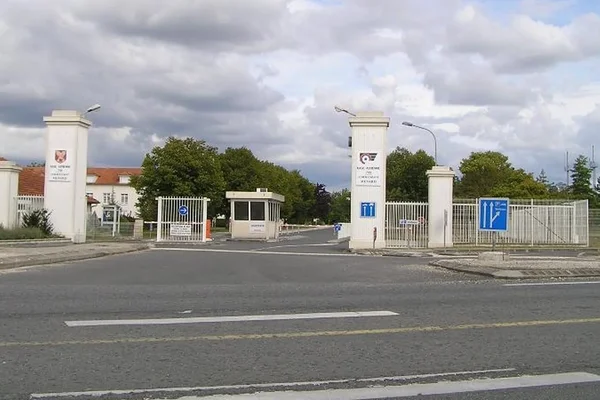 Brama wjazdowa i filary bazy lotniczej Cognac-Châteaubernard z oznaczeniami na drodze i pochmurnym niebem w tle.