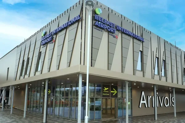 Zewnętrzna fasada terminalu Belfast International Airport z nowoczesną architekturą ze szkła i stali pod błękitnym niebem z białymi chmurami.
