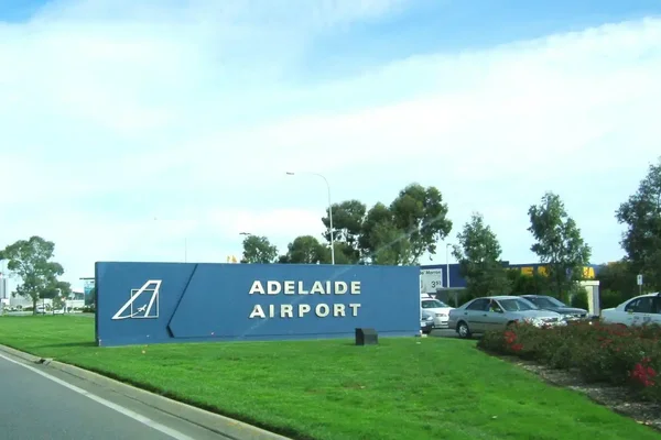 Cartello stradale per l'Aeroporto di Adelaide con sfondo blu e lettere bianche lungo un'autostrada.