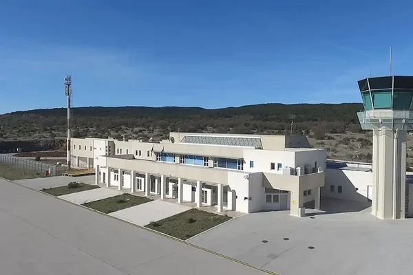 Aerial view of Brač Airport's modern white terminal building with control tower against blue sky and rocky landscape.