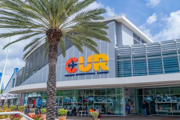 Vue extérieure du terminal de l'aéroport Hato avec palmier et signalisation colorée.