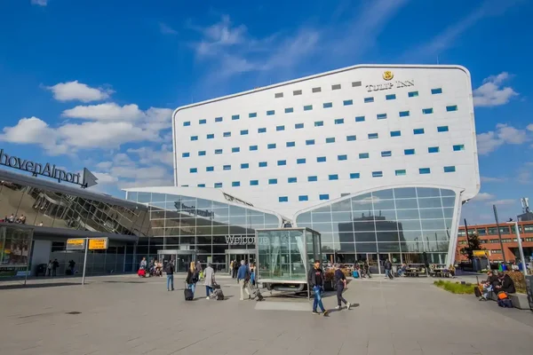 Terminal moderna del Aeropuerto de Eindhoven con fachada blanca curva bajo cielo despejado.