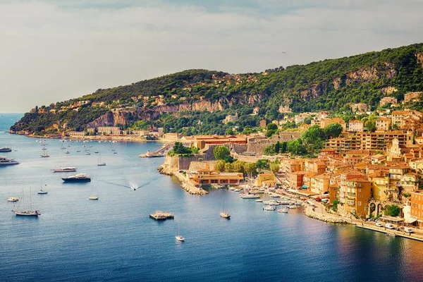 Vista aérea de la costa mediterránea cerca de Niza con yates anclados en una bahía turquesa y acantilados boscosos