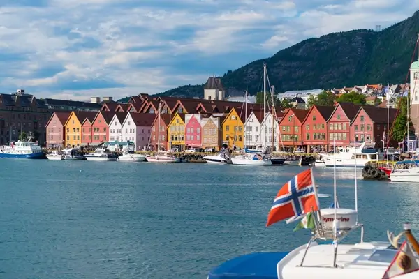 Des maisons en bois colorées bordant le quai historique de Bryggen à Bergen, en Norvège, avec des bateaux amarrés dans le port et le drapeau norvégien affiché de manière proéminente.