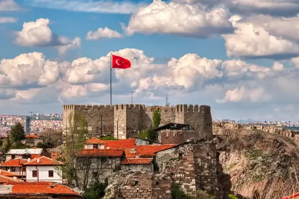 Türkische Flagge, die über historischen Steinfortressruinen mit roten Dächern und Ankara-Stadtlandschaft im Hintergrund weht