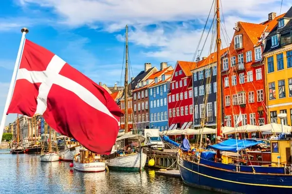 Drapeau danois flottant au-dessus de bâtiments colorés en bord de mer et de bateaux dans le quartier emblématique de Nyhavn à Copenhague