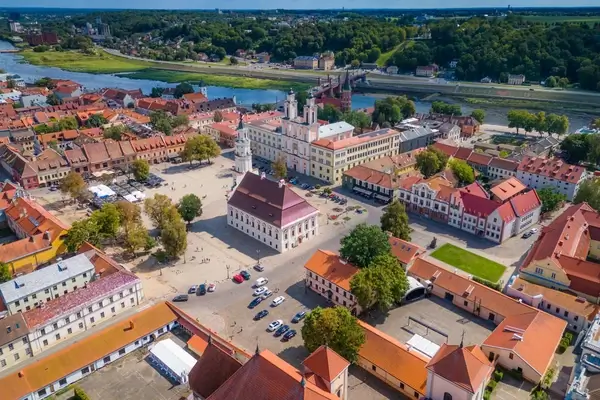 Une vue aérienne de la vieille ville de Kaunas, mettant en valeur la pittoresque place de l'Hôtel de Ville entourée de bâtiments historiques avec des toits en tuiles rouges, sur fond de la sereine rivière Neman.