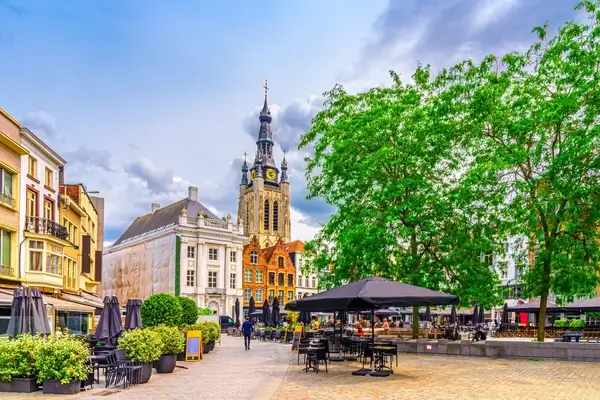 La animada plaza del mercado central en Kortrijk, Bélgica, con encantadores cafés, edificios históricos y la icónica Iglesia de San Martín, que ofrece un entorno pintoresco para los visitantes.