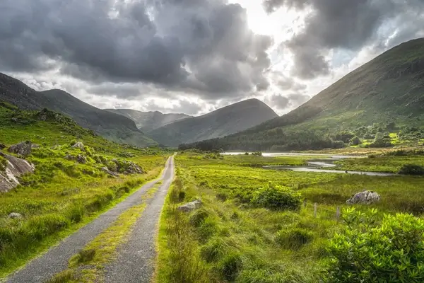 El pintoresco Valle Negro en Killarney, con una carretera sinuosa que atraviesa exuberantes colinas verdes y cielos dramáticos y nublados.