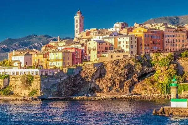 El faro de Bastia y sus coloridas casas con el mar y las montañas de fondo.