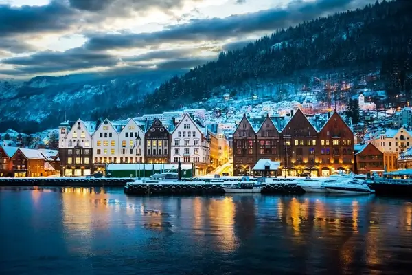 Bryggen waterfront à Bergen, Norvège au crépuscule avec des bâtiments historiques colorés et des montagnes enneigées reflétées dans l'eau du fjord
