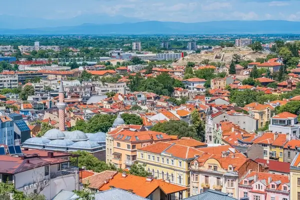 Aerial view of Zemun, Serbia with red-roofed buildings, the Danube River, and distant mountains under blue sky