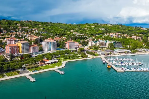 Aerial view of a Mediterranean coastal town with turquoise waters, marina, and hillside residential buildings