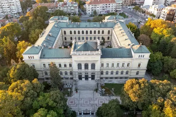 Aerial view of a grand neoclassical government palace with symmetrical architecture, courtyards, and manicured grounds surrounded by autumn foliage